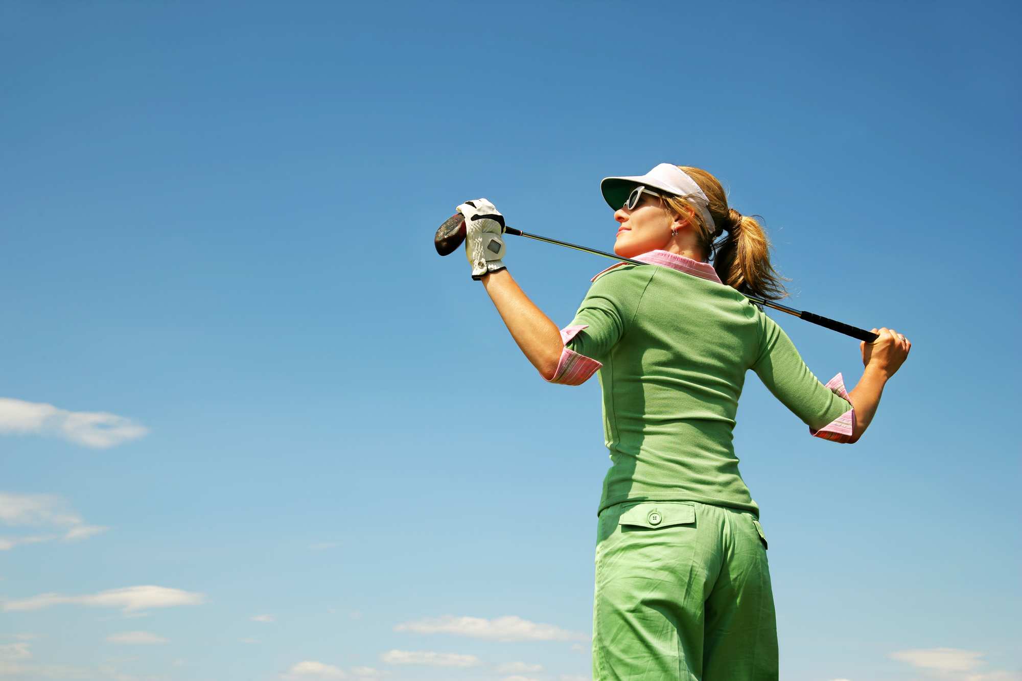 A woman en green golf shirt holding an golf club up her back